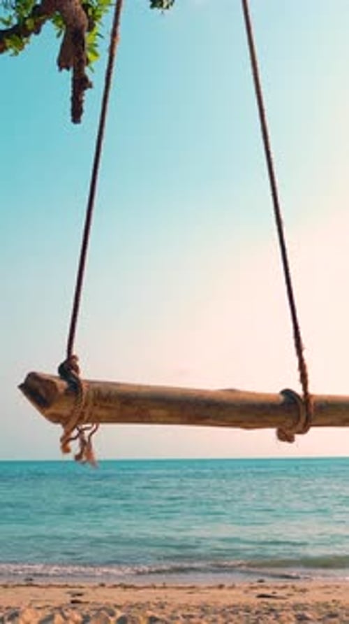 Enjoying a peaceful swing by the serene beach at sunset. Vertical video