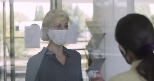 Business people arriving in corporate office lobby wearing protective face mask