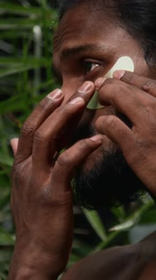 Homem indiano bonito aplicando hidrogel sob tapa-olhos na floresta tropical