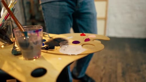 Nahaufnahme in einem Kunstworkshop: Ein Künstler in einem blauen T-Shirt trägt weiße Farbe auf eine Palette mit einem