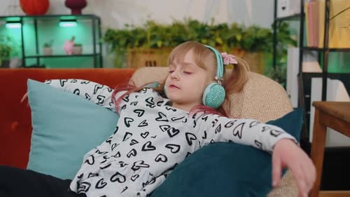 Girl Listens to Music on Headphones, Reclining on Couch