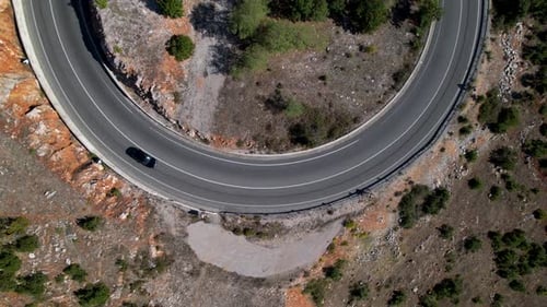 Black car driving on curve of mountain road, top down zoom aerial view, travel concept