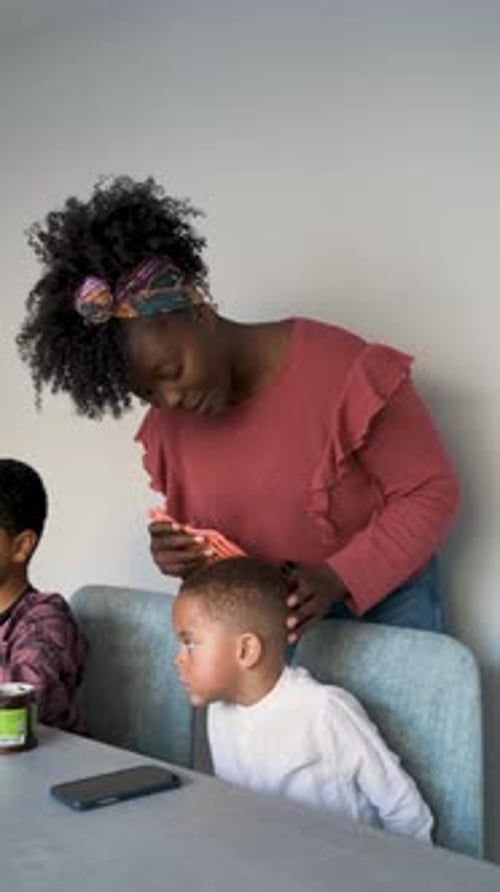 Woman Combs Child's Hair at Table Indoors