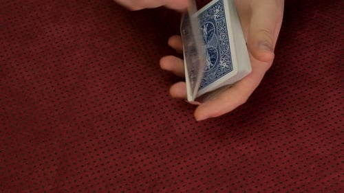 Hands Manipulating Playing Cards on Red Table