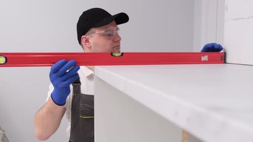 Un artisan professionnel en uniforme vérifie le panneau du meuble avec un niveau