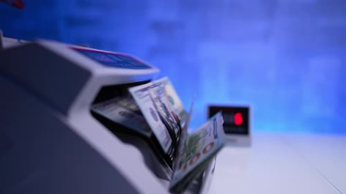 Female hand puts a stack of one hundred dollar bills into the modern money counting device.