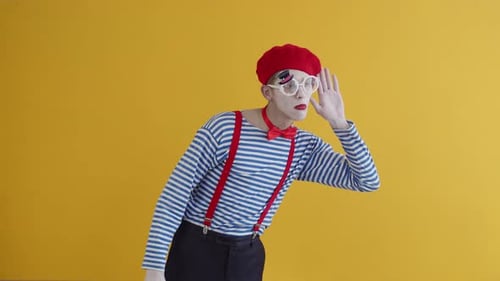 A Young Mime Guy Pretends to Be Eavesdropping Putting His Palm to His Ear and is Surprised Covering