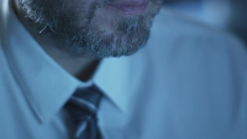 Manager is working on a computer in the evening in a dark office room filled with display screens.