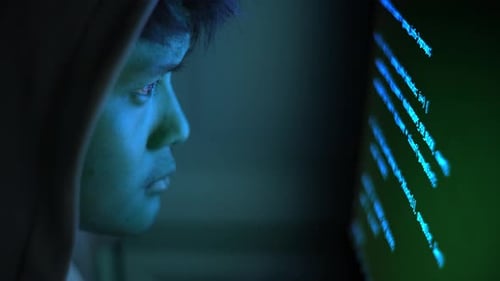Hacker im Kapuzenpulli codiert am Computerbildschirm in dunkelblauer Cybersicherheitseinstellung