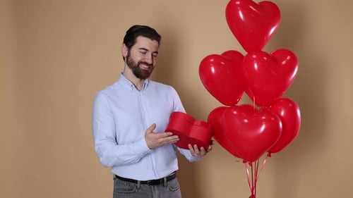 St. Valentine's Day. Man with gift and heart shaped balloons on beige background