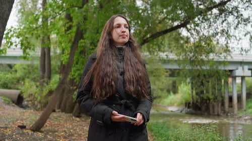 Individual Walking Along River Bridge Woman with Curly Hair Under Overcast Autumn Sky Female Figure