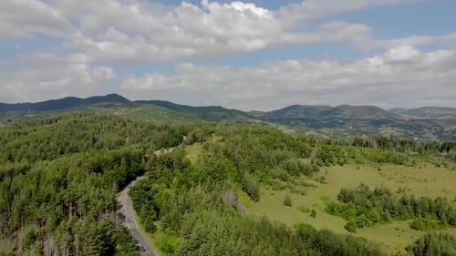Flying over an empty road surrounded by trees in the mountains with clouds in the sky