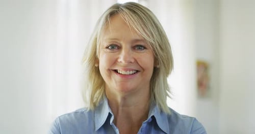 Authentic close up of an attractive mature blond hair woman with blue eyes is smiling in camera in