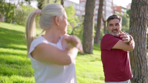 Senior Couple Stretching Arms Exercising Outdoors in a Park