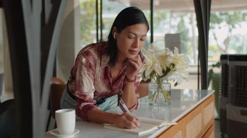Woman Writing in Notebook at Marble Countertop