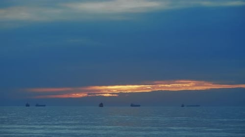 Steady sunset shot of cargo ships sailing in calm sea near port in Portugal.