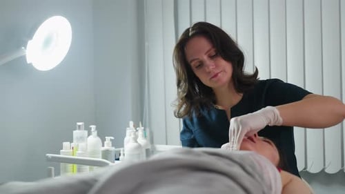 Aesthetician Dipping Fingernail And Cradling Client Jawline During Spa Session