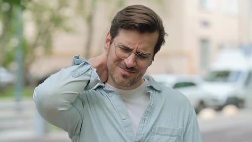 Man Rubs Stiff Neck Outdoors in the City