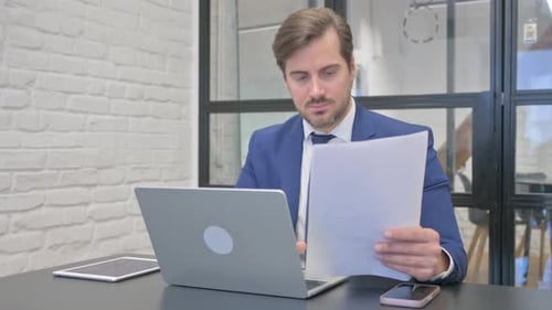Man Reviews Documents and Types on Laptop