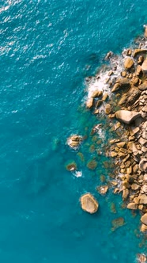 Stunning rocky shoreline meeting bright blue ocean waves. Vertical video