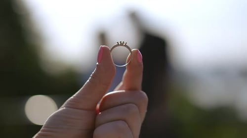 Nahaufnahme Eine Frau betrachtet einen Verlobungsring, den sie mit zwei Finger hält, vor dem Hintergrund von