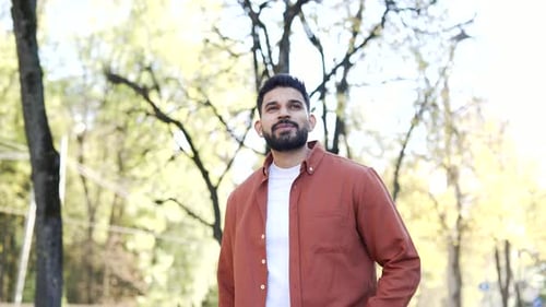 Happy businessman walking on urban city park. Smiling confident bearded man in red shirt walks