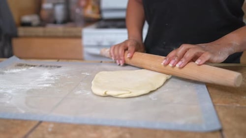 Hands Rolling Dough with Pin in Kitchen