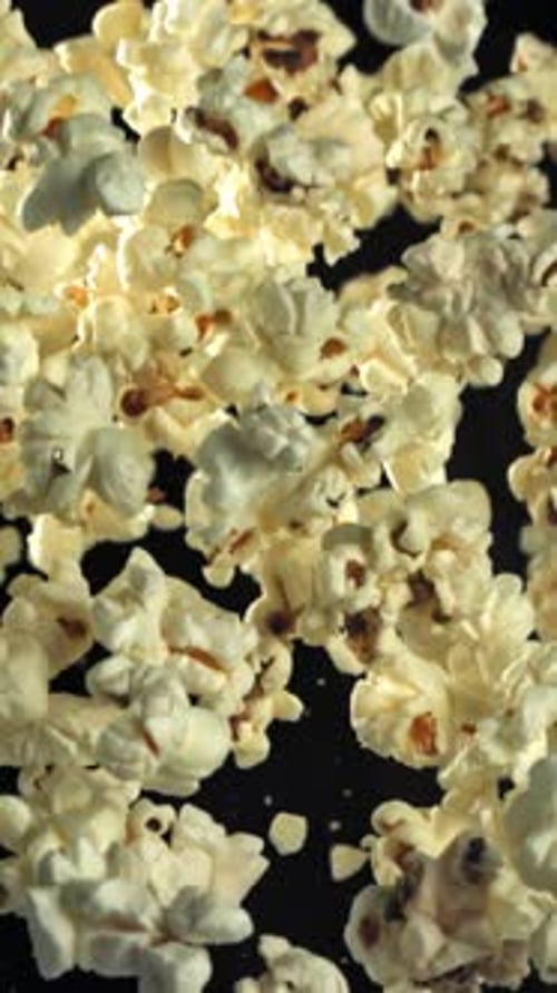 Popcorn fliegt hoch und fällt auf einem schwarzen Hintergrund herunter, gefilmt mit einer Hochgeschwindigkeitskamera mit 1000 Bildern pro Sekunde