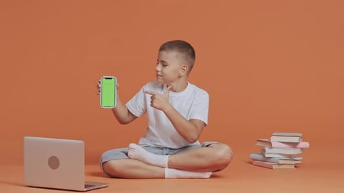 A Young Schoolboy Points to Smartphone with Green Screen Chroma Key