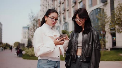 Young Women Using Phone Together in City