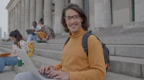 Portrait of Handsome Student with Laptop Sitting on Stairs Outside University