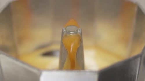 Slow motion pour of moka pot coffee from metal spout, brewing process close-up