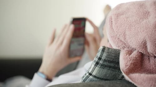 A woman after a shower with a towel on her head lies on the couch and looks at the phone.