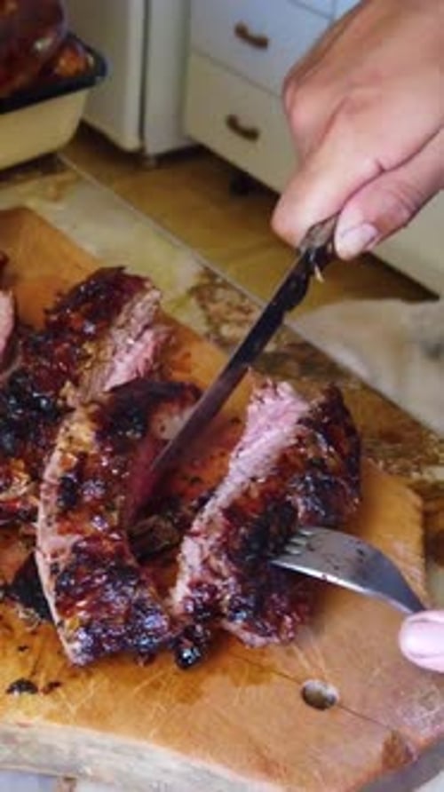 Vertical close up hands cutting asado red meat with knife, traditional argentine and south american