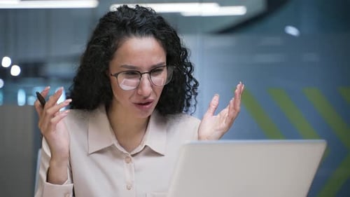 Angry businesswoman arguing talking on a video call using laptop in office. Frustrated female