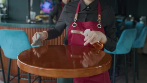 Unrecognizable Waitress Using Spray to Disinfect Tables for Guests in Cafe