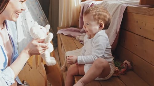 Young Woman Giving Plush Toy To Baby, Both Smiling