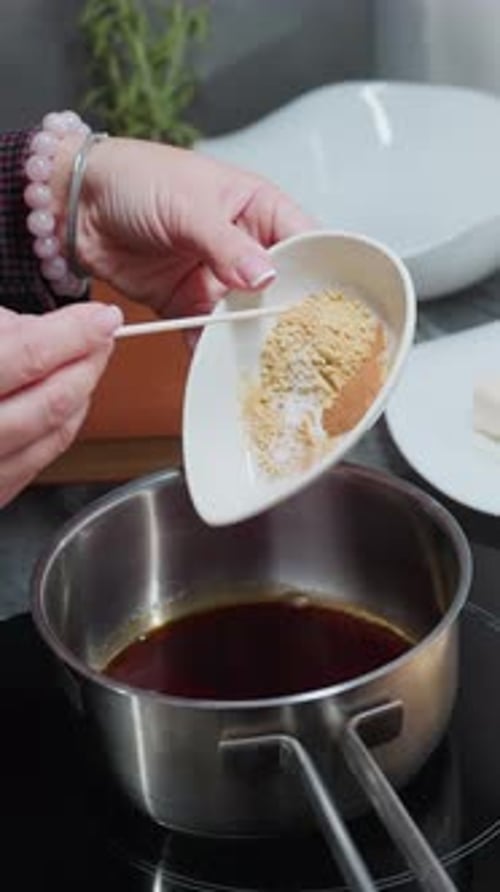 Woman adds spices to liquid in saucepan indoors