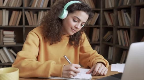 Woman Studying and Writing at Desk with Headphones