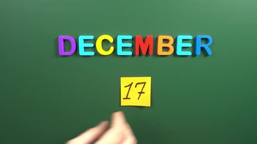 Hand sticking a sticker 17 December calendar day on school board. 17 date of December. Seventeenth
