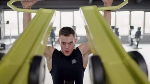 Concentrated Man Works on Lever Trainer for Back Muscle in Spacious Fitness Club