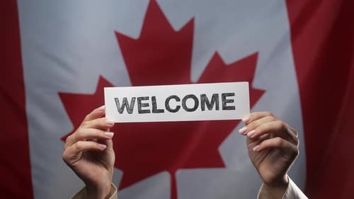 Hands Hold Welcome Sign Over Canadian Flag