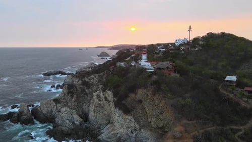 Pull front approaching a small lighthouse and cliff with sun at sunset