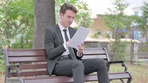 Man Reviews Documents on Park Bench in Suit