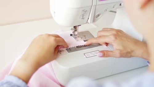 Woman clothing designer sews pink fabrics on a sewing machine. Needlework and handmade