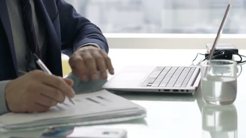 Young Businessman Working with Documents and Laptop Sitting by Desk in Office Adult