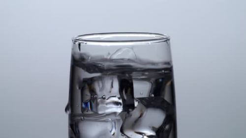 Close Up Of Ice Cubes Falling In A Glass Of Drinking Water On The Light White Screen Background