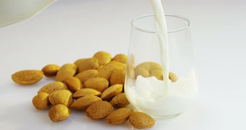 The almond milk is poured into a glass in slow motion, the background in woods there are almonds,