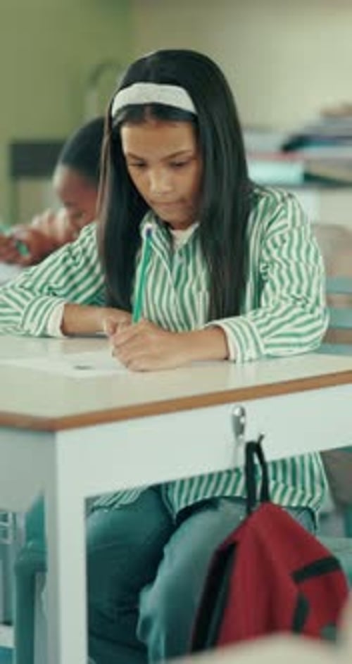 Girl Writes at School Desk in Classroom