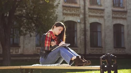 Young Woman Writing on Bench in Sunny City Park